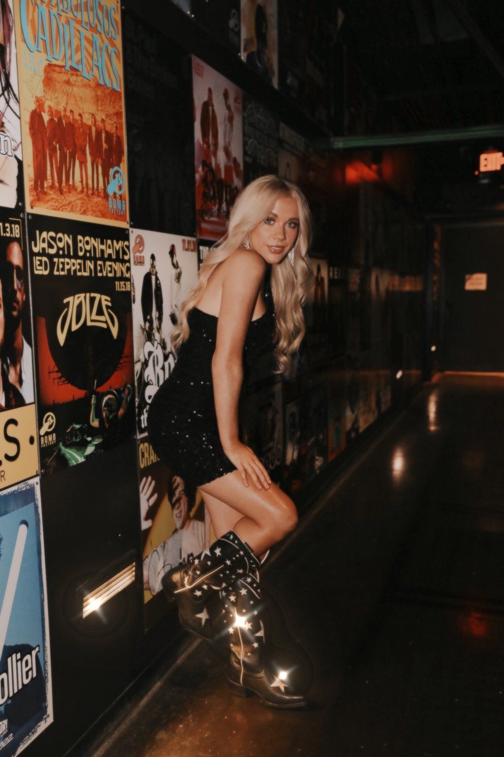 A stylish nightlife photo near a wall covered in concert posters and neon lights.