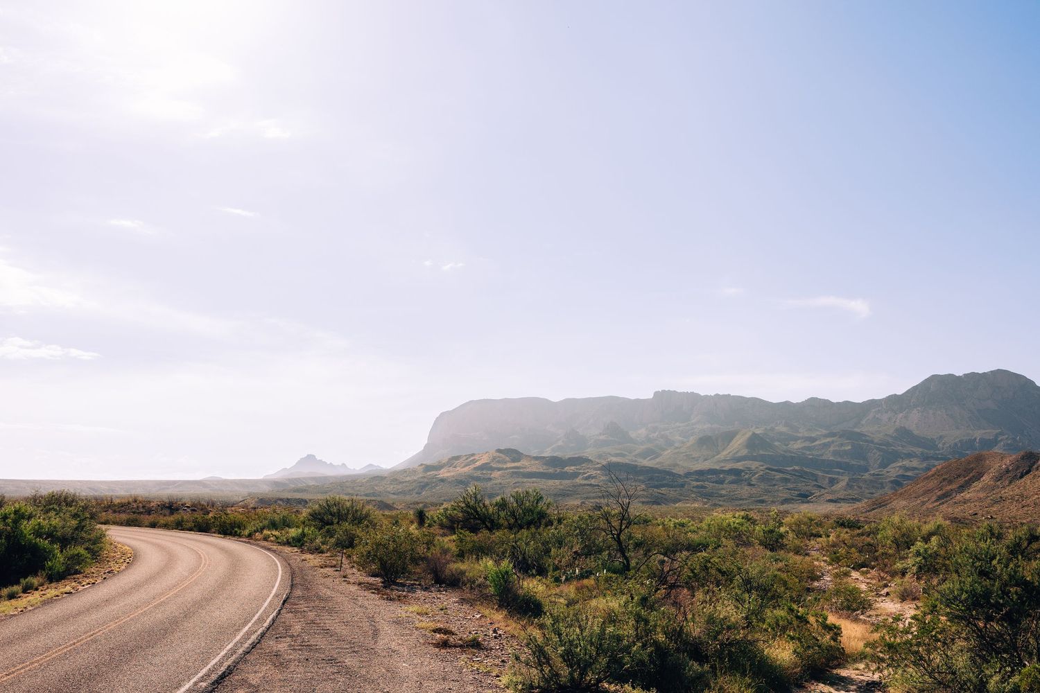 Scenic panoramic view of winding desert road through rugged mountain landscape under bright blue sky.