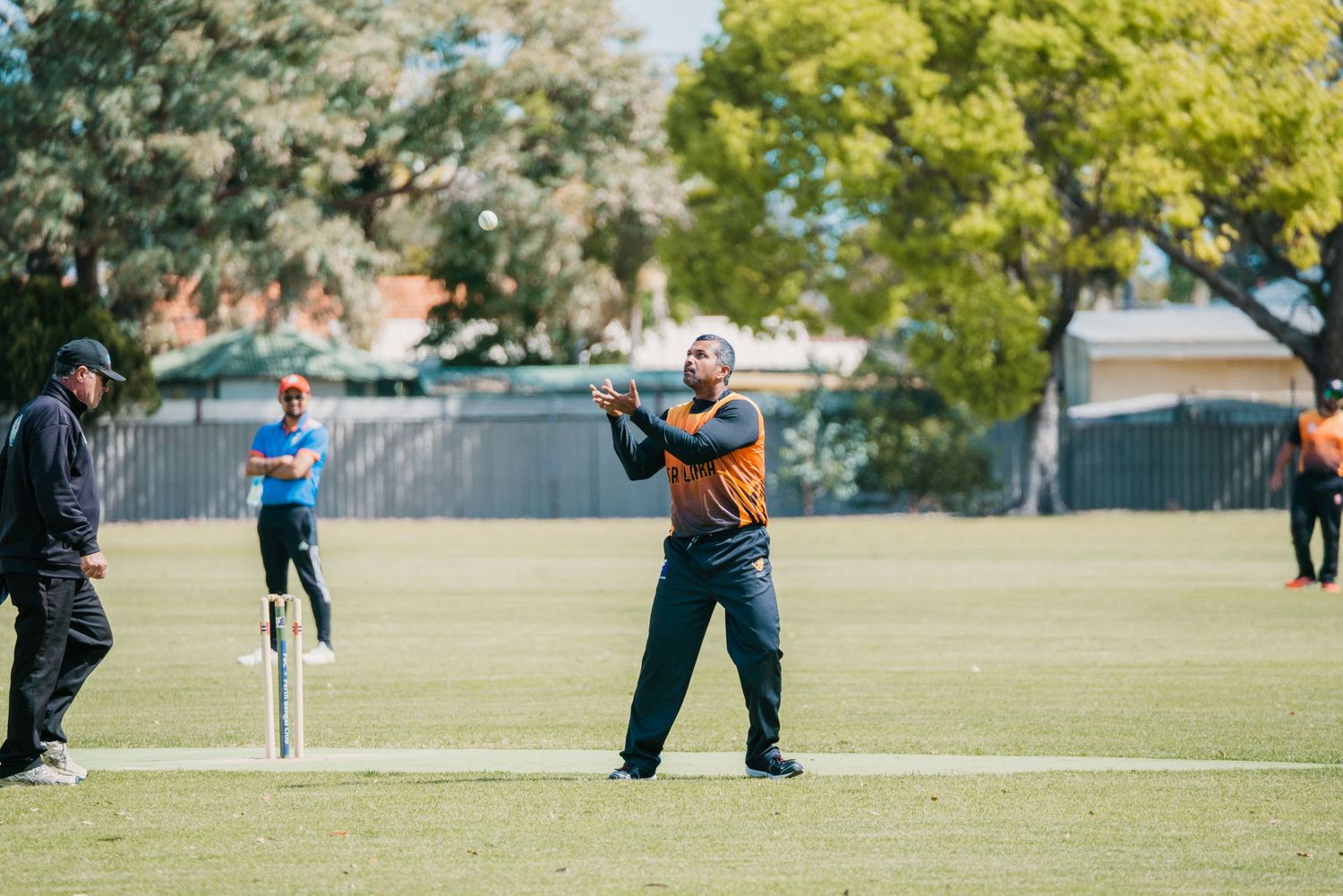 Cricket player in orange uniform catching a ball on a green field during an outdoor match.