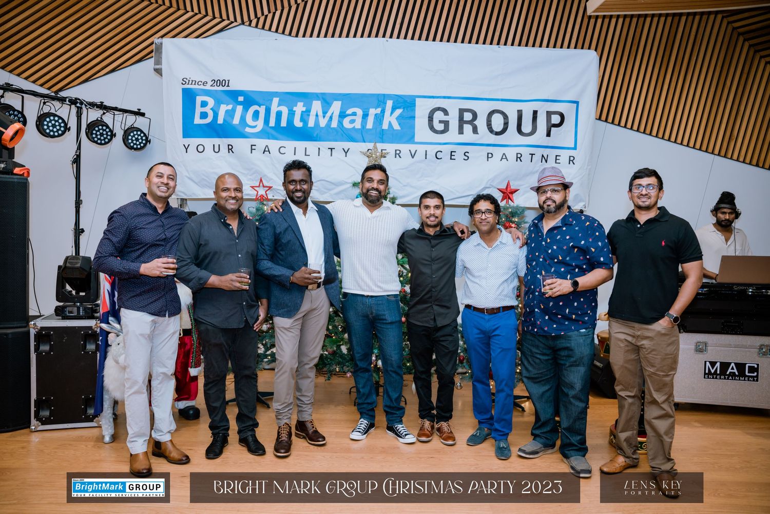 A group of eight men posing in front of the BrightMark Group banner at Christmas Party 2023.