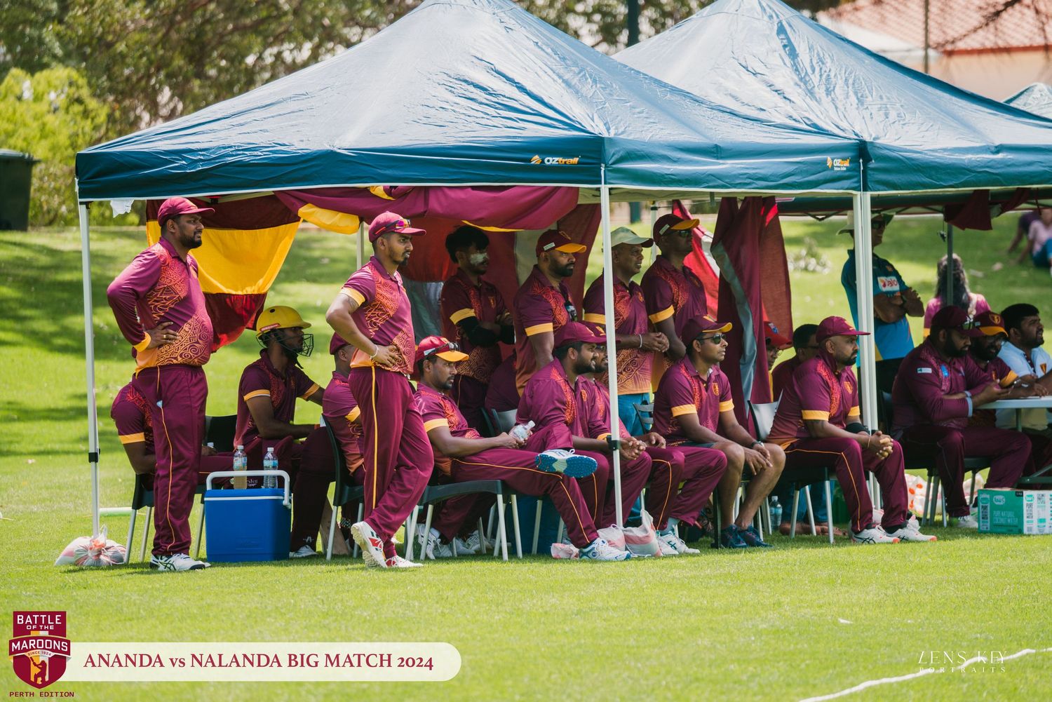 Cricket team in maroon uniforms resting under blue tents during Ananda vs Nalanda Big Match 2014.