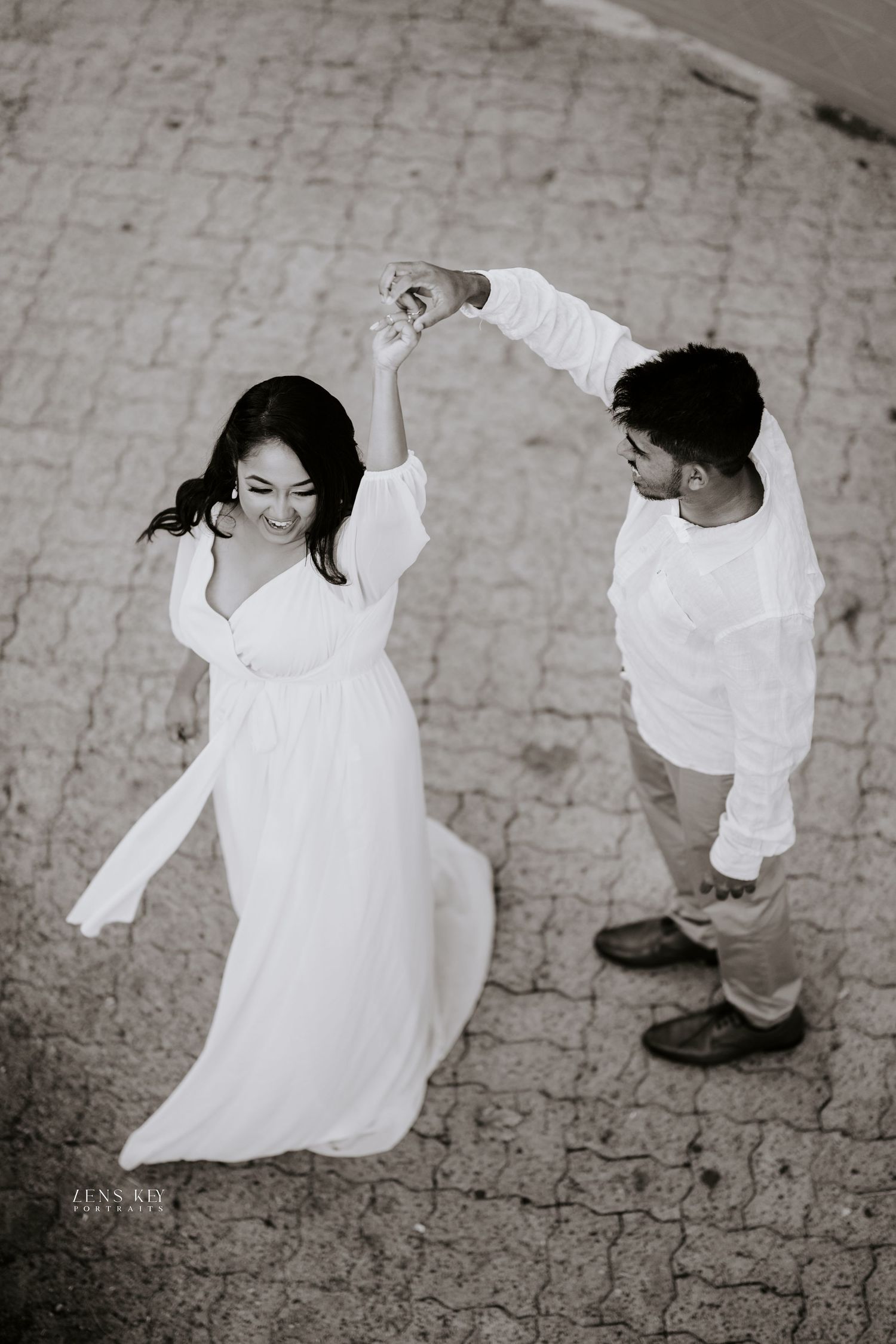 Black and white aerial shot of couple dancing outdoors, groom spinning bride in flowing white dress.