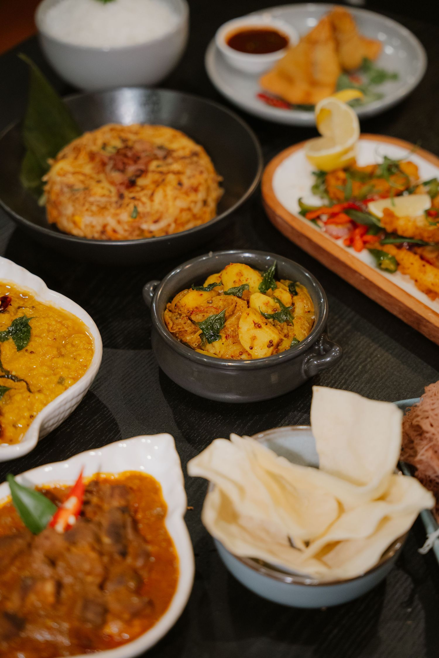 A spread of Indian dishes including biryani, curry, dal, papadums, and samosas on a dark table.