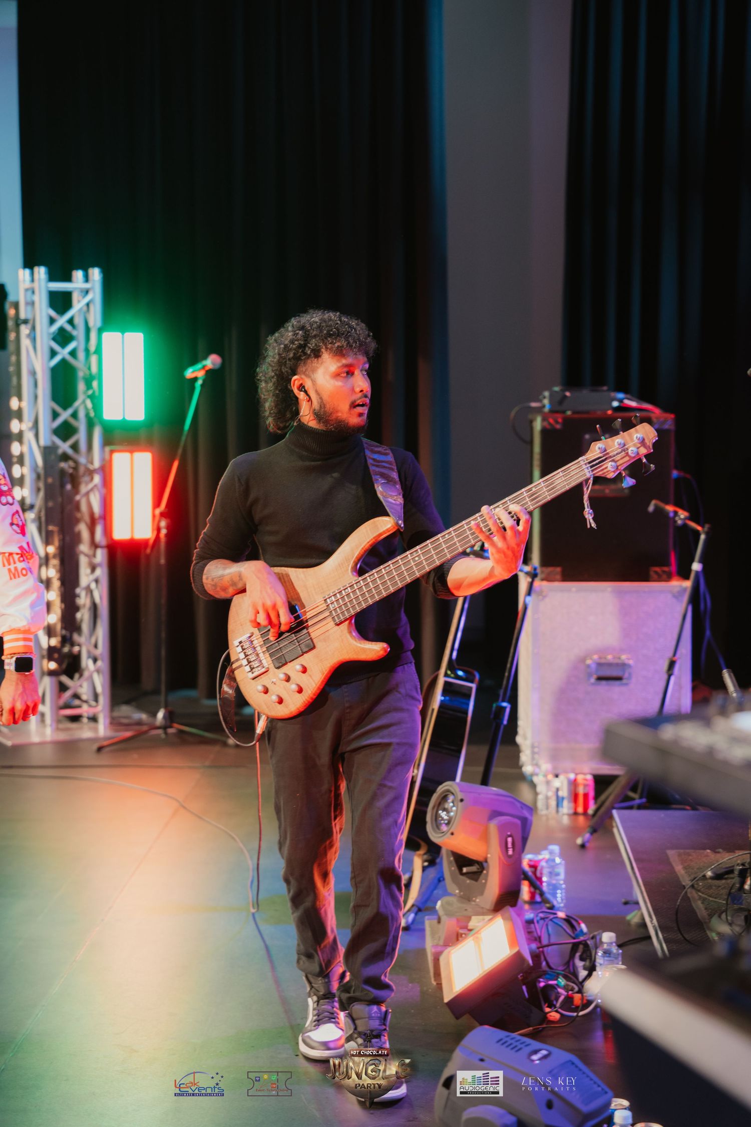 Male bassist playing five-string bass guitar on stage under warm concert lighting.