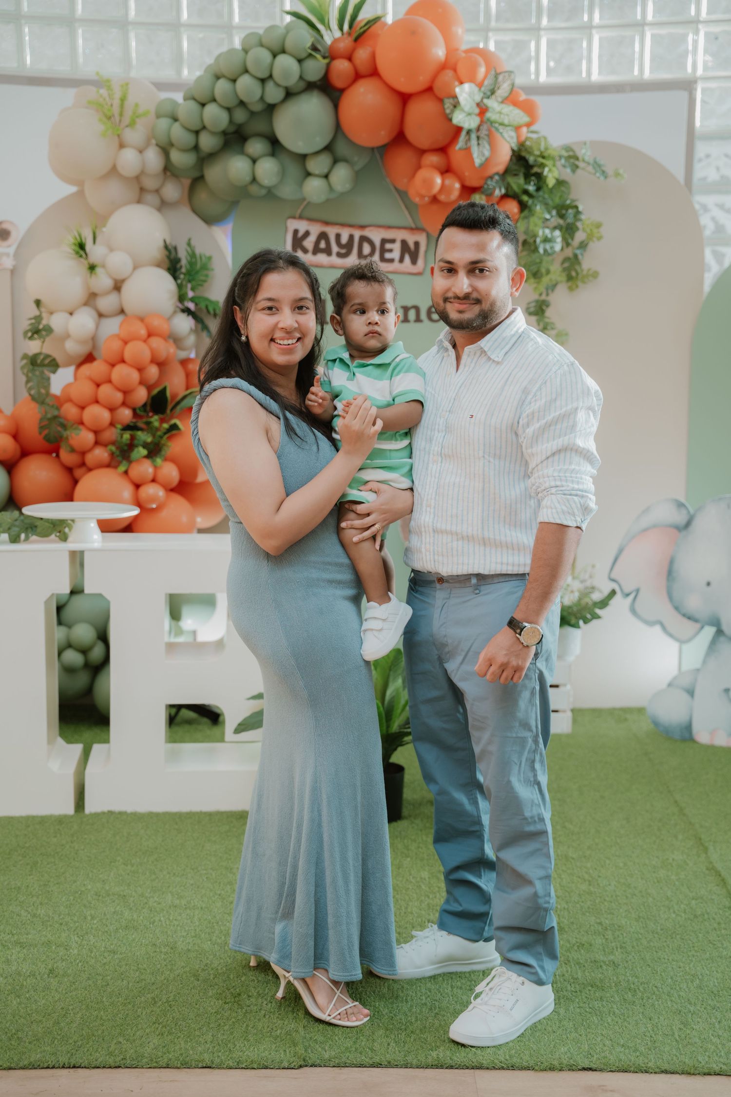 A family of three poses together at baby Kayden's Wild One first birthday party with colorful balloon arch.