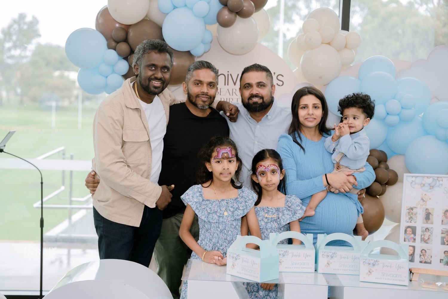 Group of friends posing at a baby's first birthday party with balloon decorations.