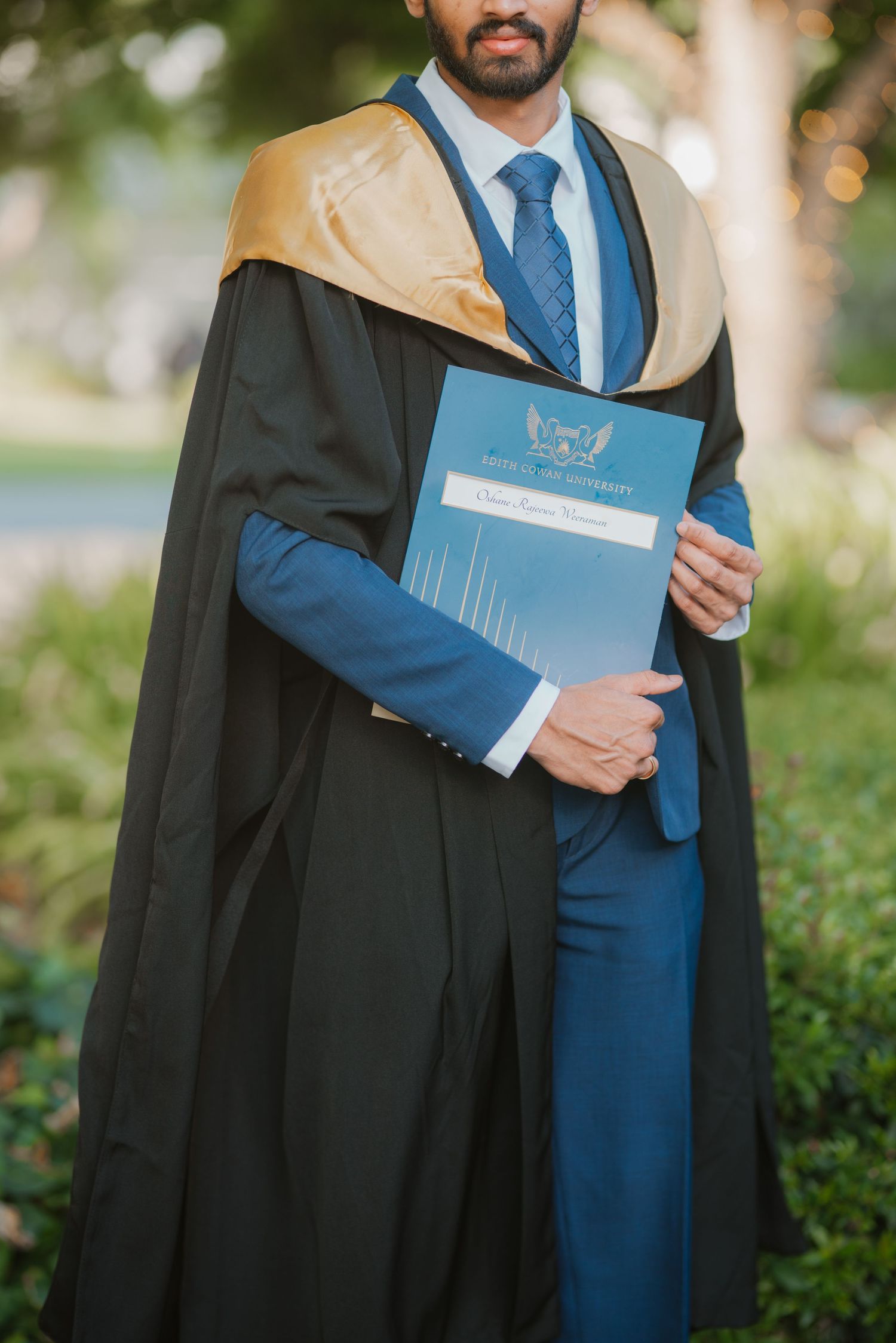 Close-up of male graduate in black and gold gown holding university diploma certificate.
