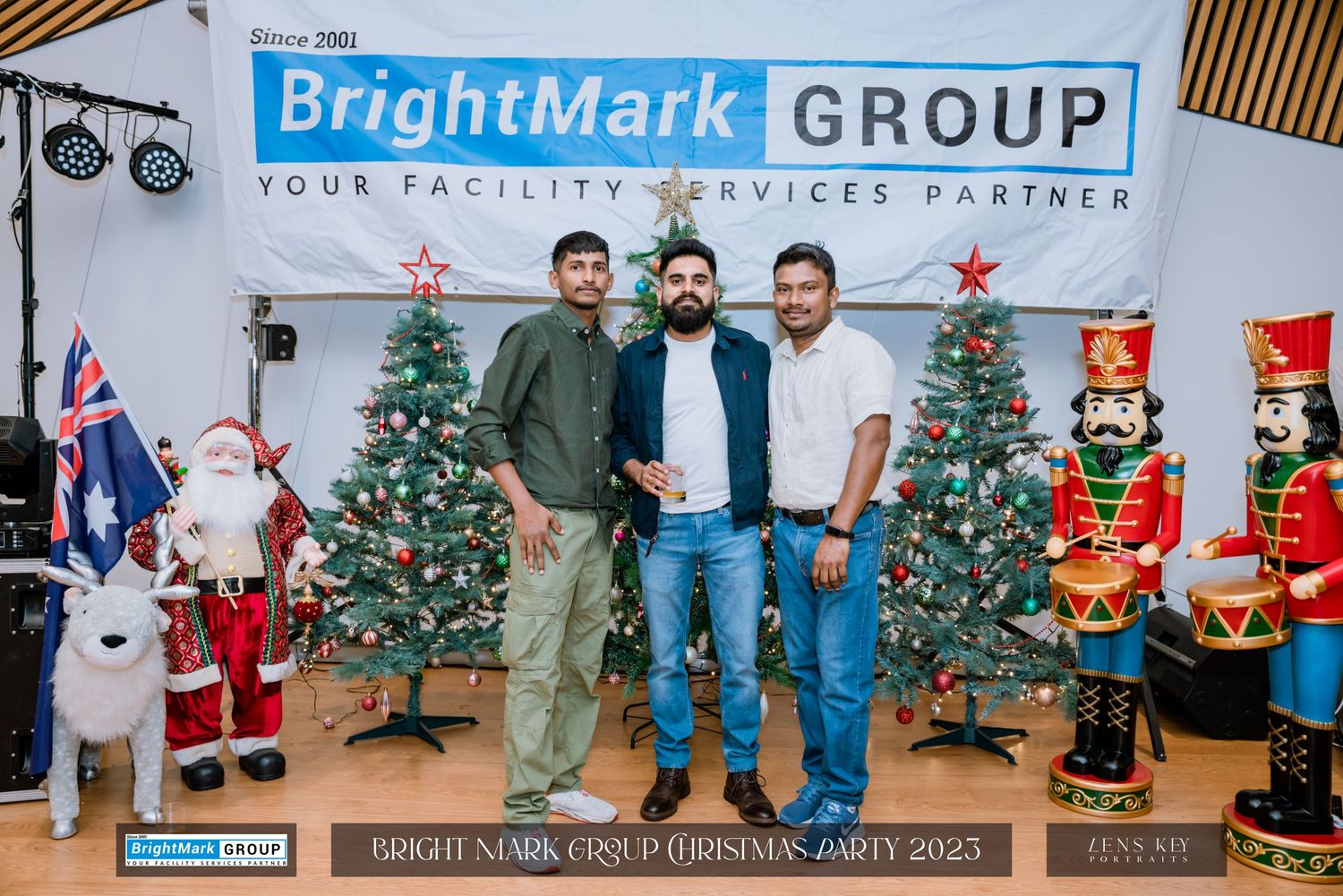 Three men posing together in front of Christmas trees at BrightMark Group Christmas Party 2023.