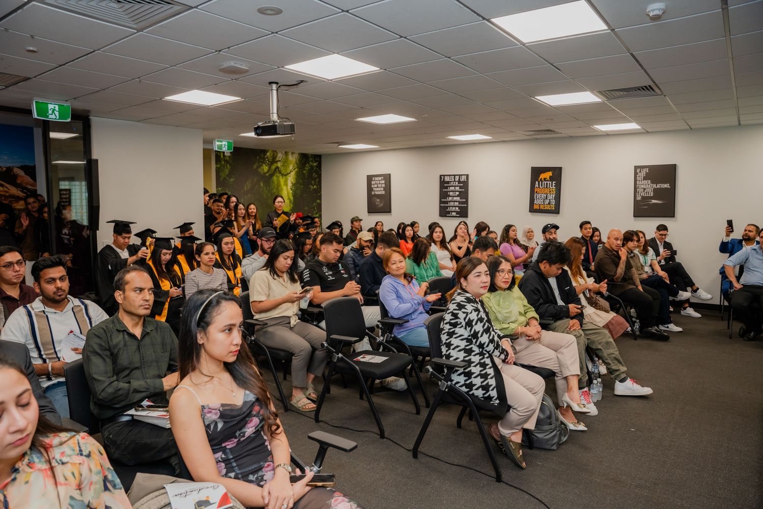 Large audience seated in rows at an indoor graduation or academic ceremony event.