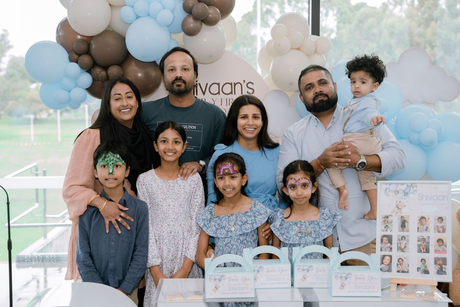 Large family group photo at a first birthday party with balloon arch backdrop.