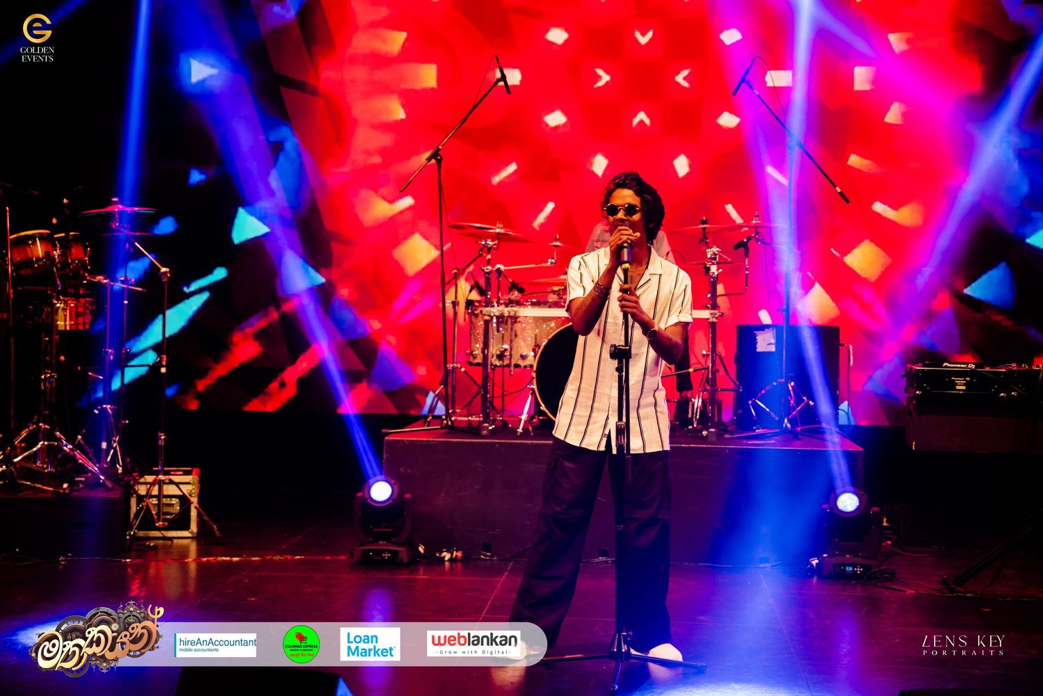 Male singer performing solo on colorfully lit stage with geometric light display backdrop.