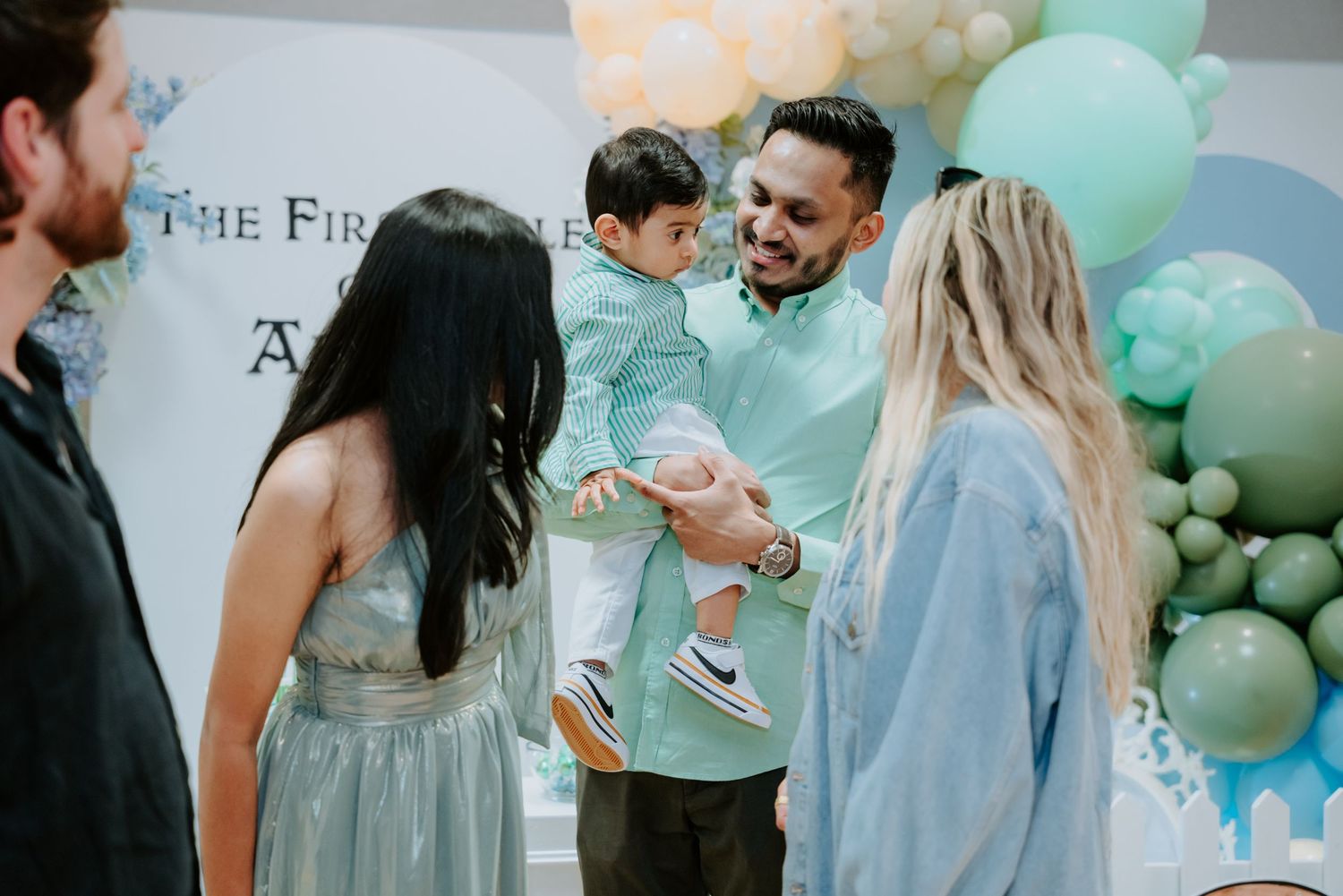 A man holds a young child while chatting with guests at a blue themed first birthday party.