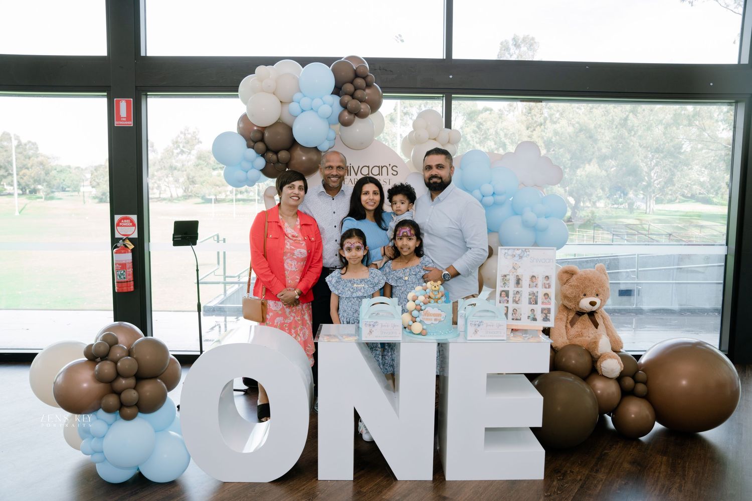 Family celebrating baby's first birthday beside large ONE letter decorations and balloons.