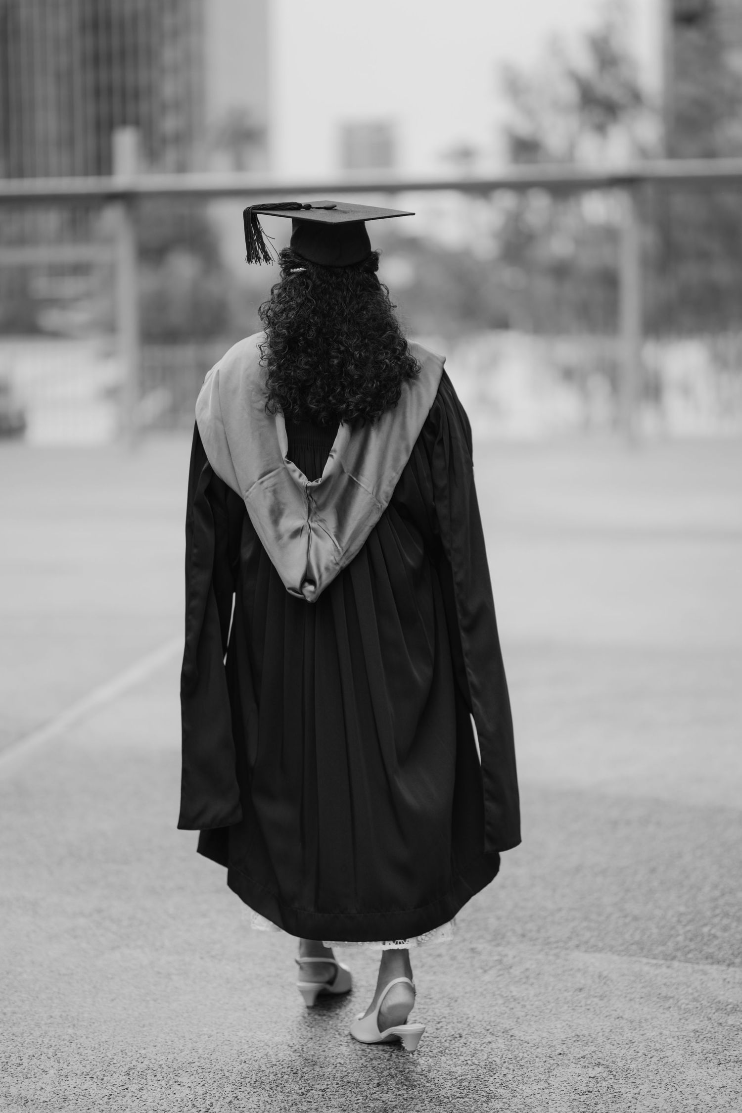 Black and white rear view of graduate in cap and gown walking away on campus.