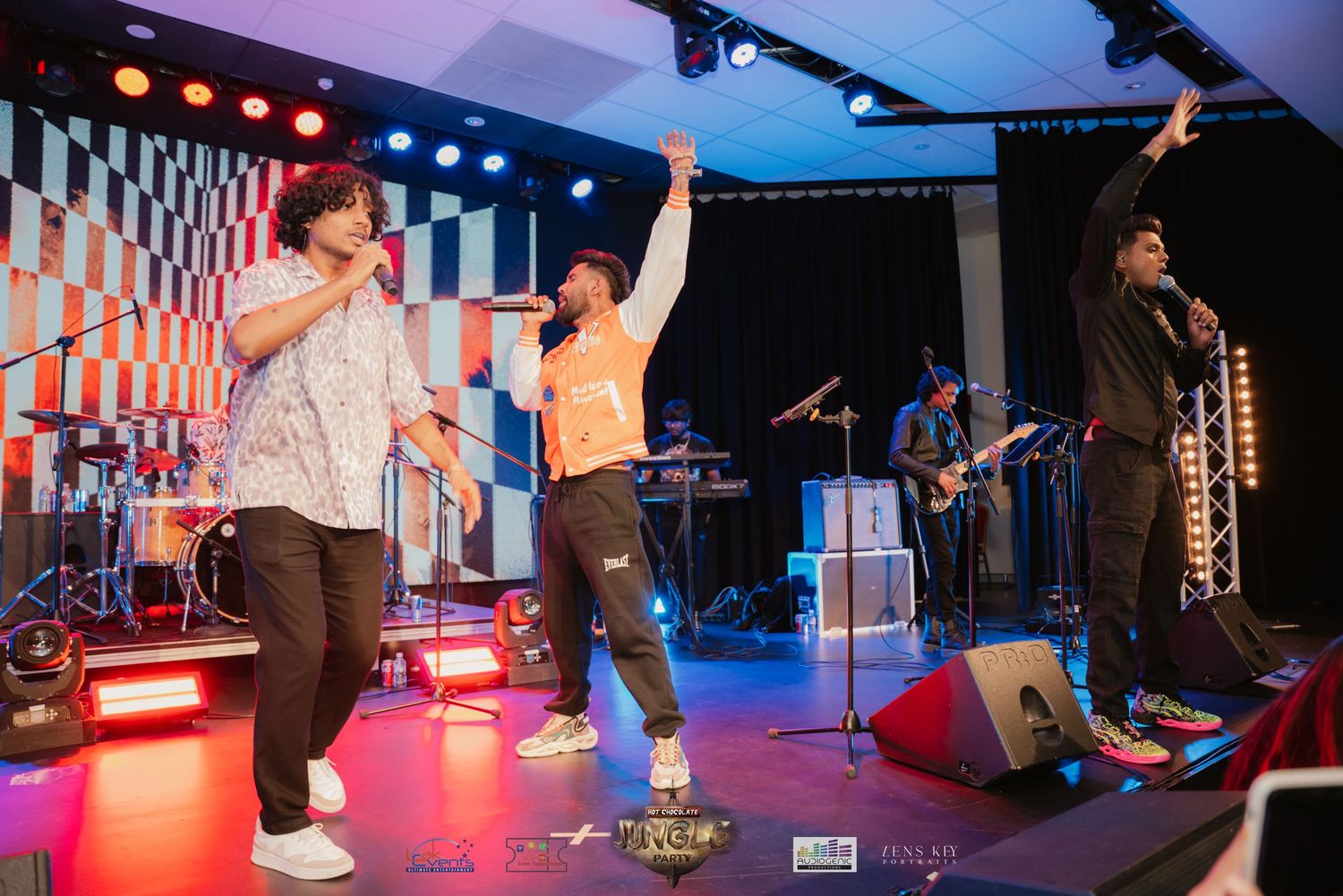 Three performers dancing on stage with a live band during an energetic show.