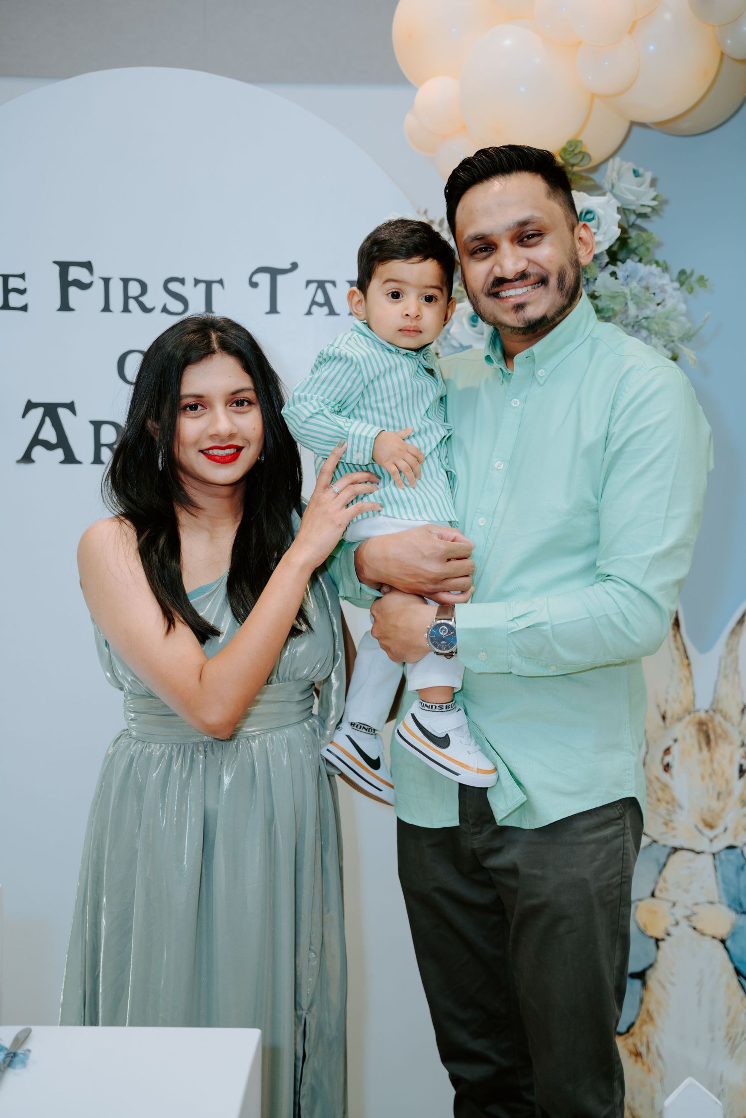 Family of three in matching mint outfits poses at Peter Rabbit themed first birthday celebration.