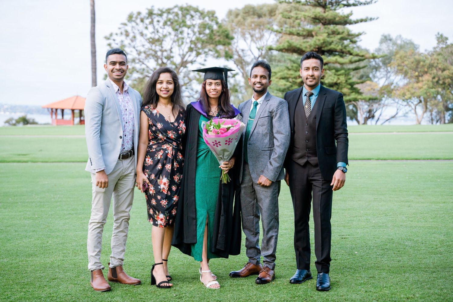 A proud graduate in green regalia poses with four family members on a lush green lawn.