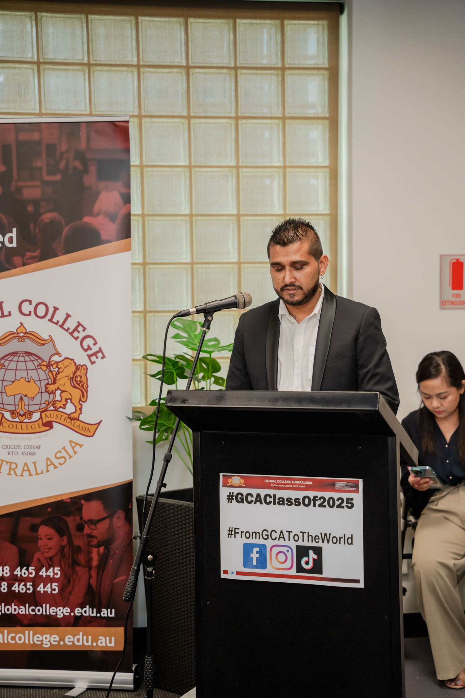 A man in a suit speaking at a podium at a Global College Australasia graduation ceremony.