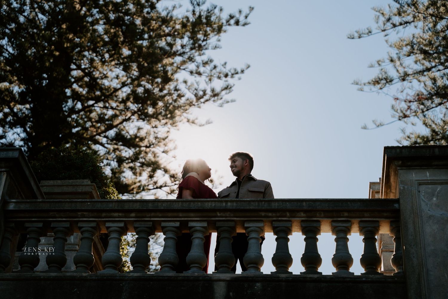 Romantic couple silhouetted against golden sunset light on a classic stone balustrade terrace.