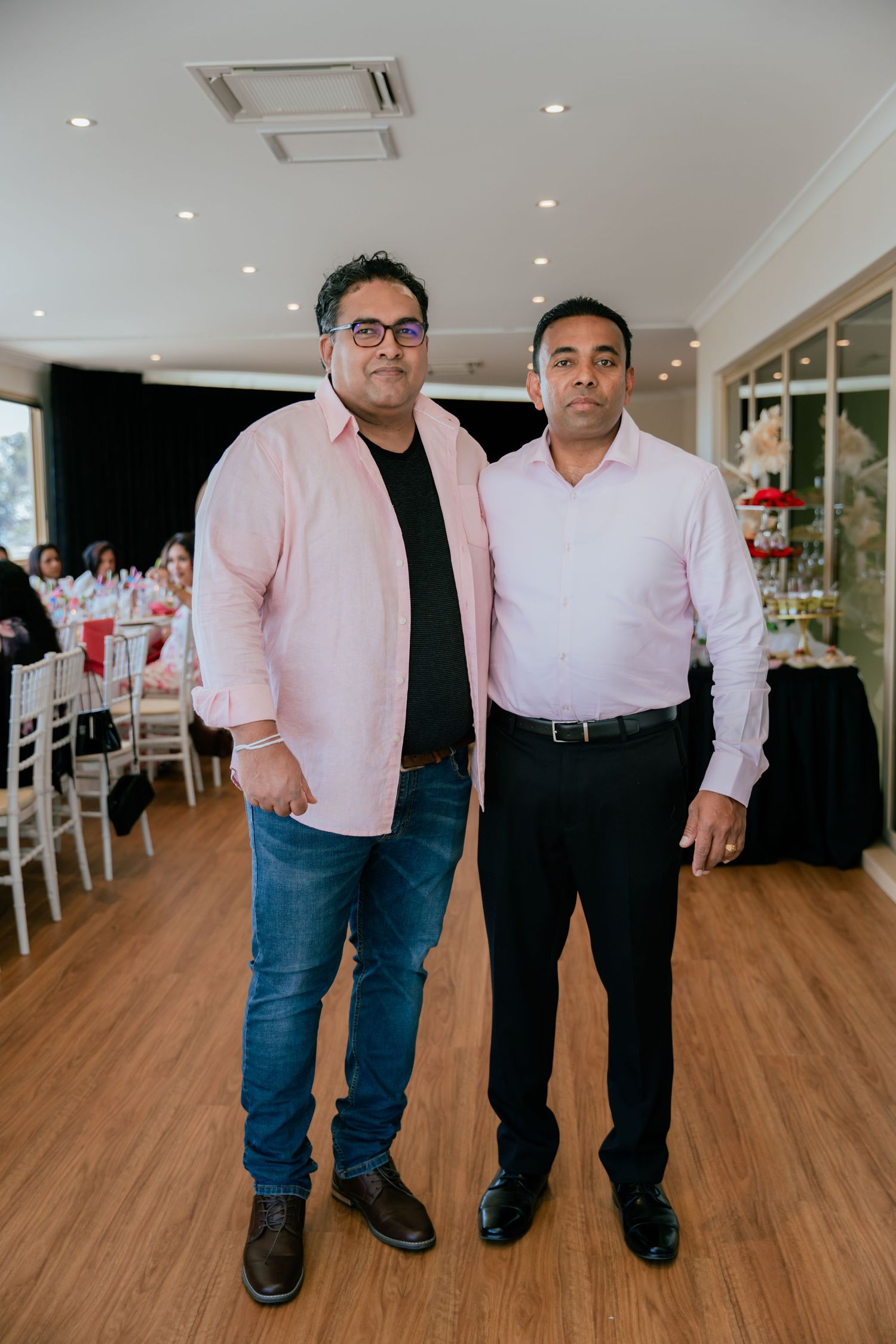 Two men in pink shirts pose together at an elegant birthday party celebration venue.