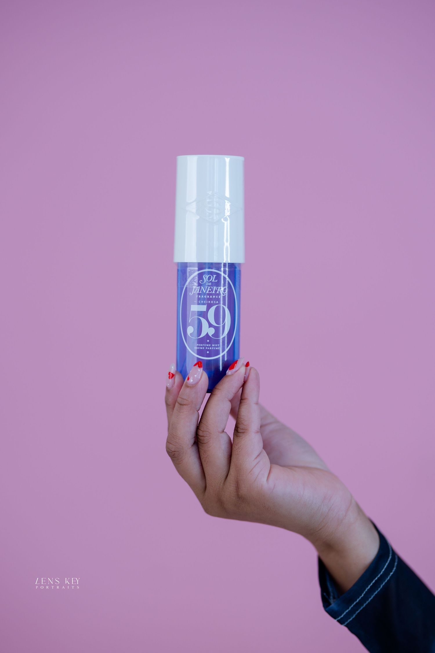 Hand holding a blue and white FarmHouse Fresh 59 skincare serum bottle against a pink background.