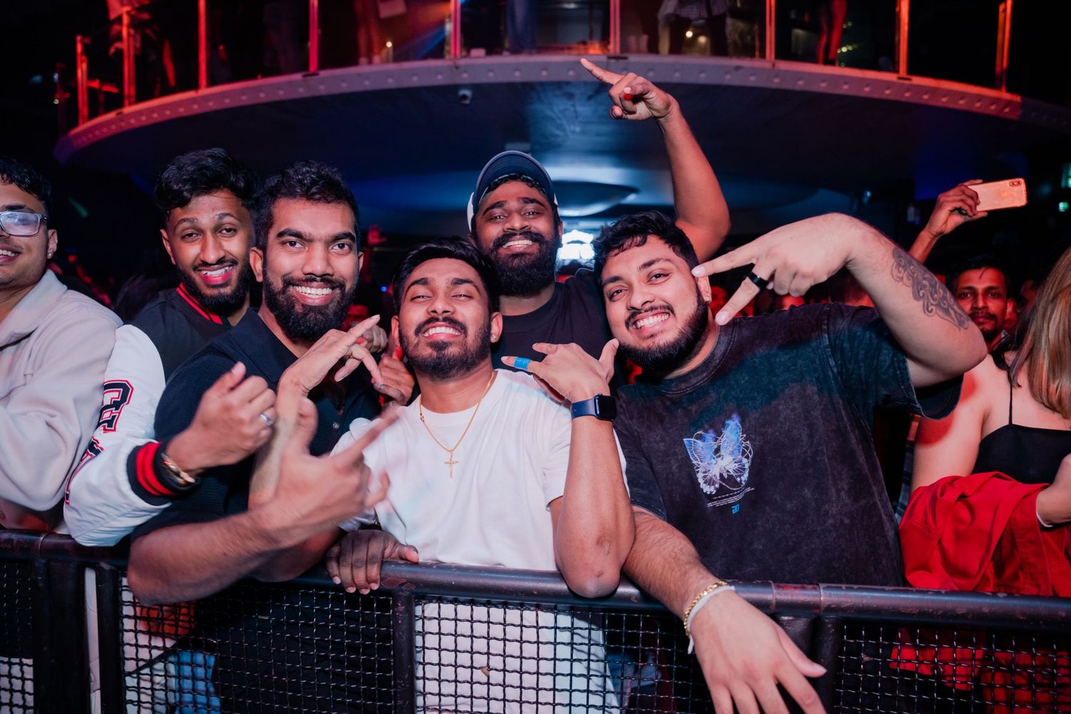 Group of five friends posing together at a nightclub with purple lighting.