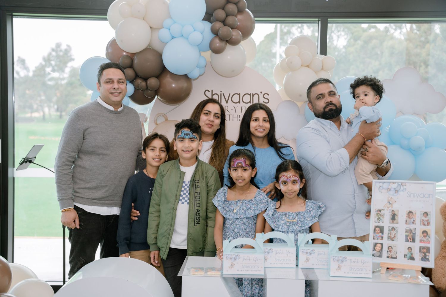 Family group photo at Shivaan's first birthday party with balloon arch backdrop.