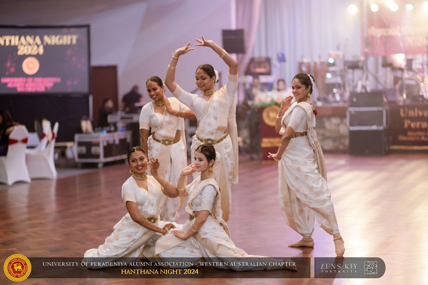 Traditional dancers in white costumes performing graceful moves on a stage at a cultural gala night.
