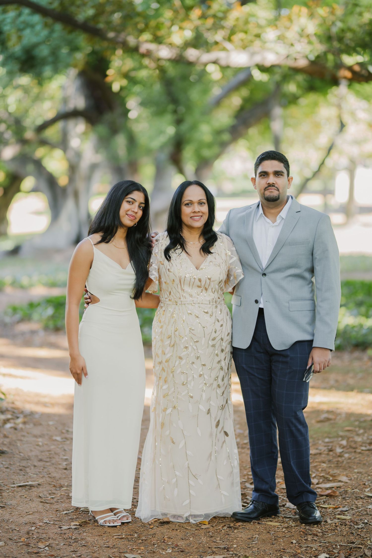 Woman in gold embroidered gown poses with daughter in white dress and son in grey blazer outdoors.