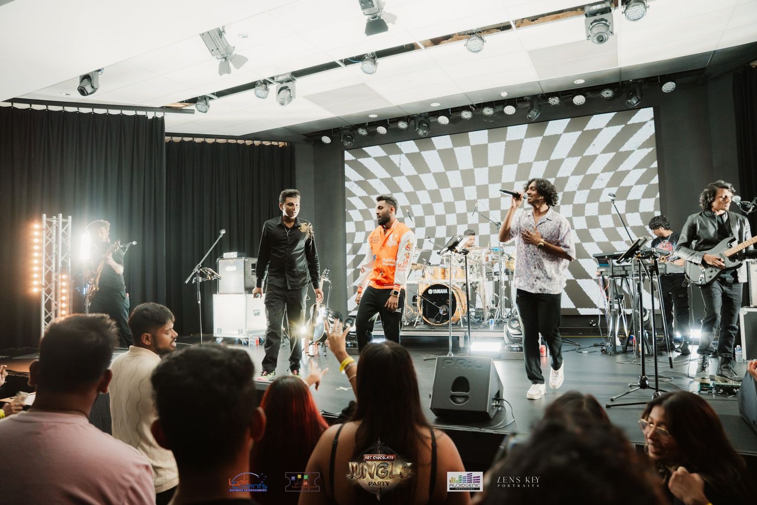 Band performing on checkered stage with audience watching in an intimate venue.