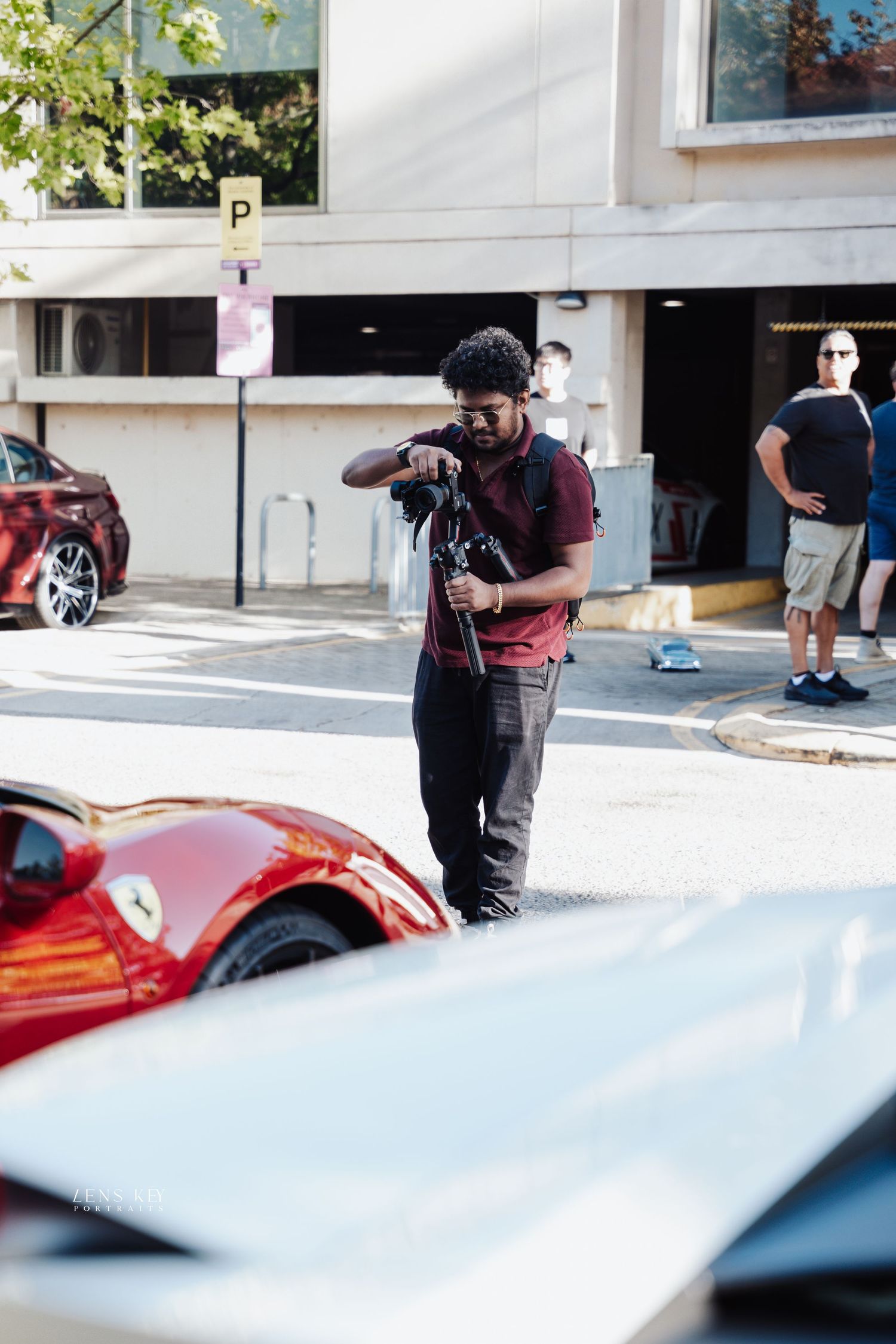 Man photographing a red Ferrari sports car at an outdoor car show on a sunny day.