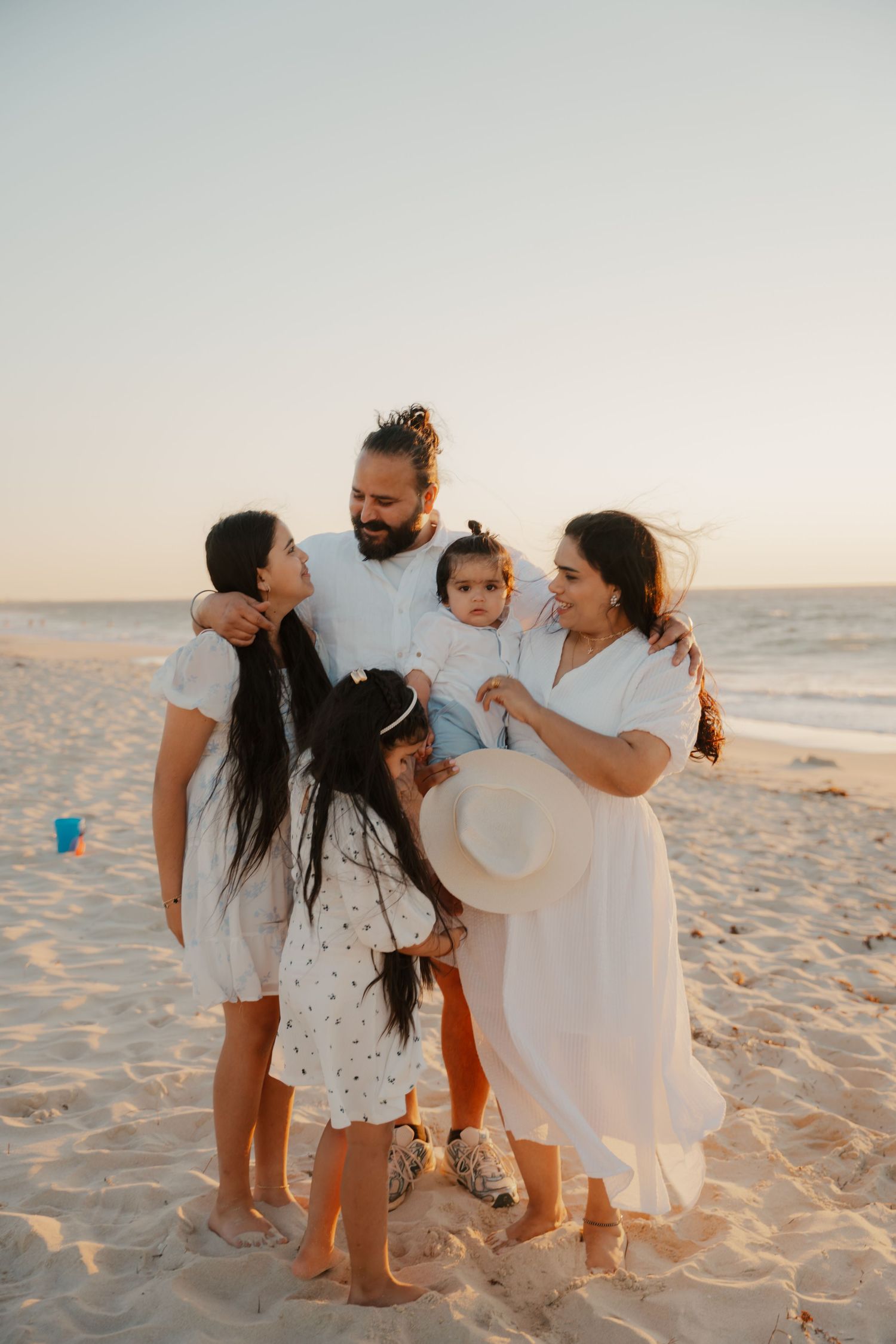 Joyful family of five laughing and bonding together on sandy beach during golden sunset.