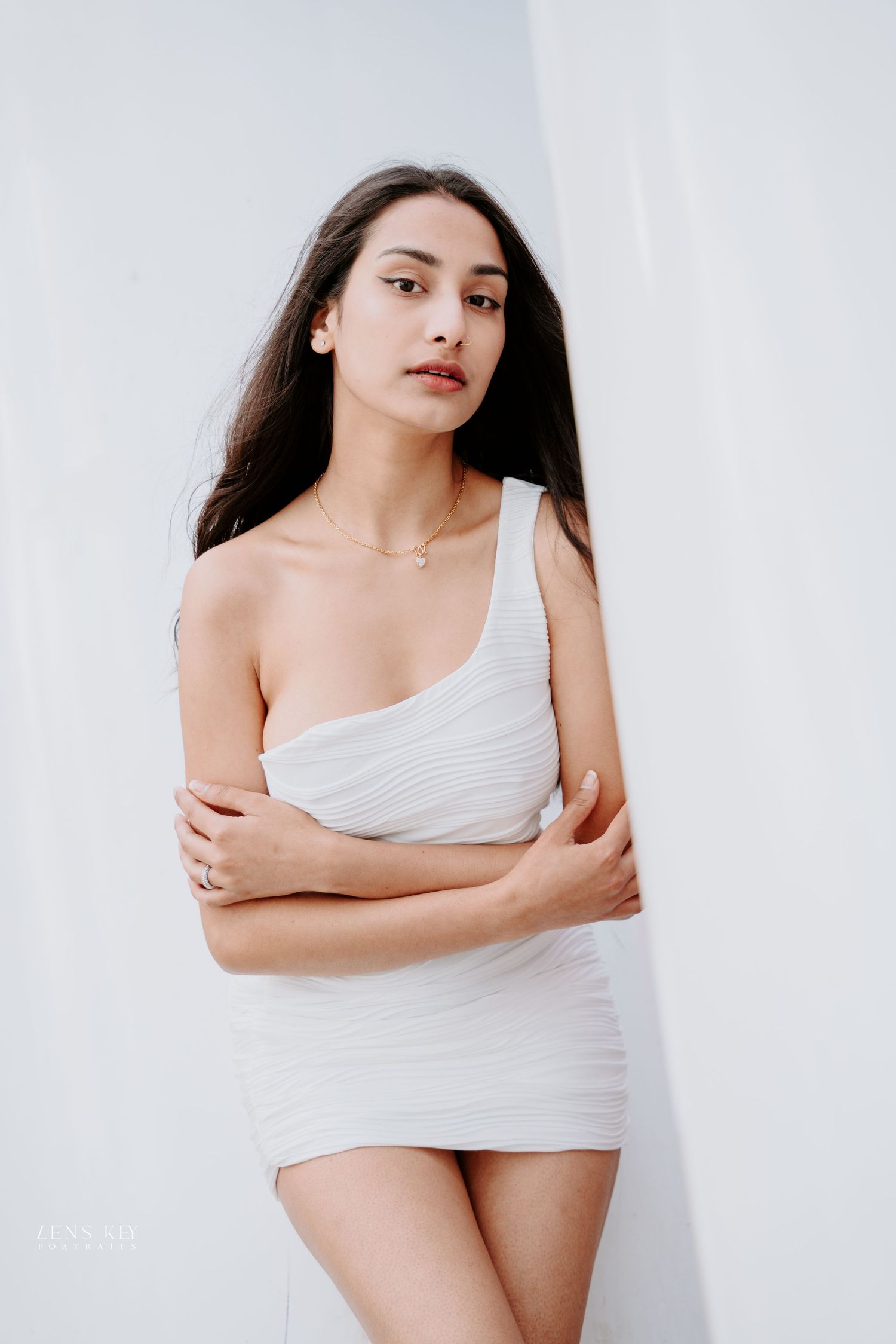 Young woman in white one-shoulder ribbed mini dress posing against white background.