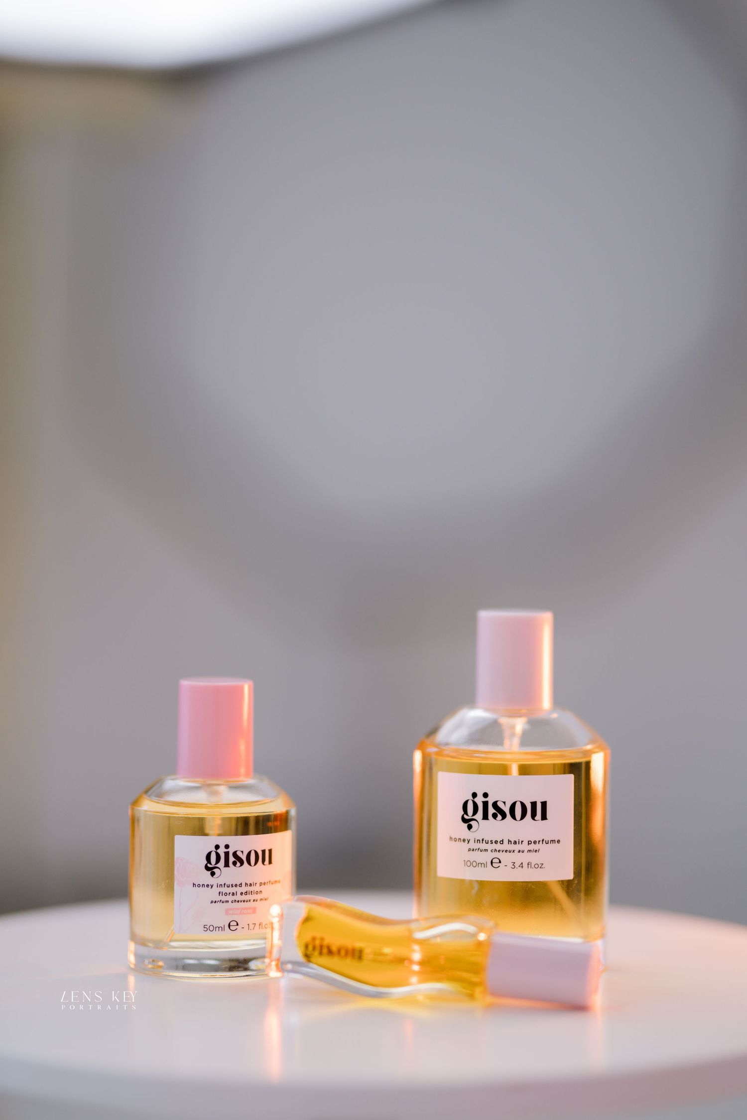 Two Gisou honey infused hair perfume bottles in small and large sizes displayed on white round table.
