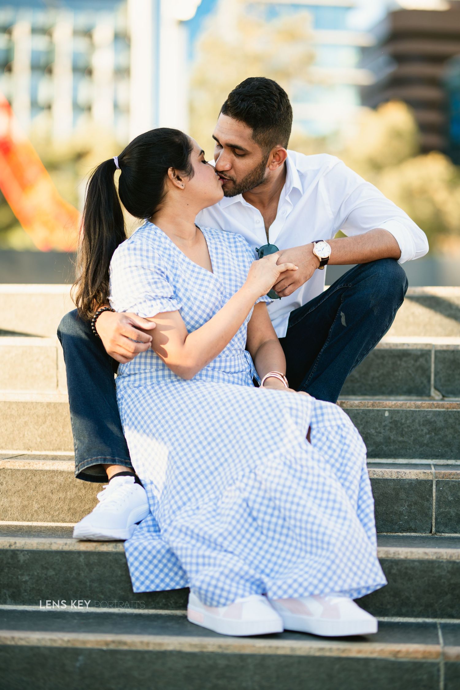 Couple sharing a kiss while sitting on steps during an outdoor engagement photo shoot.