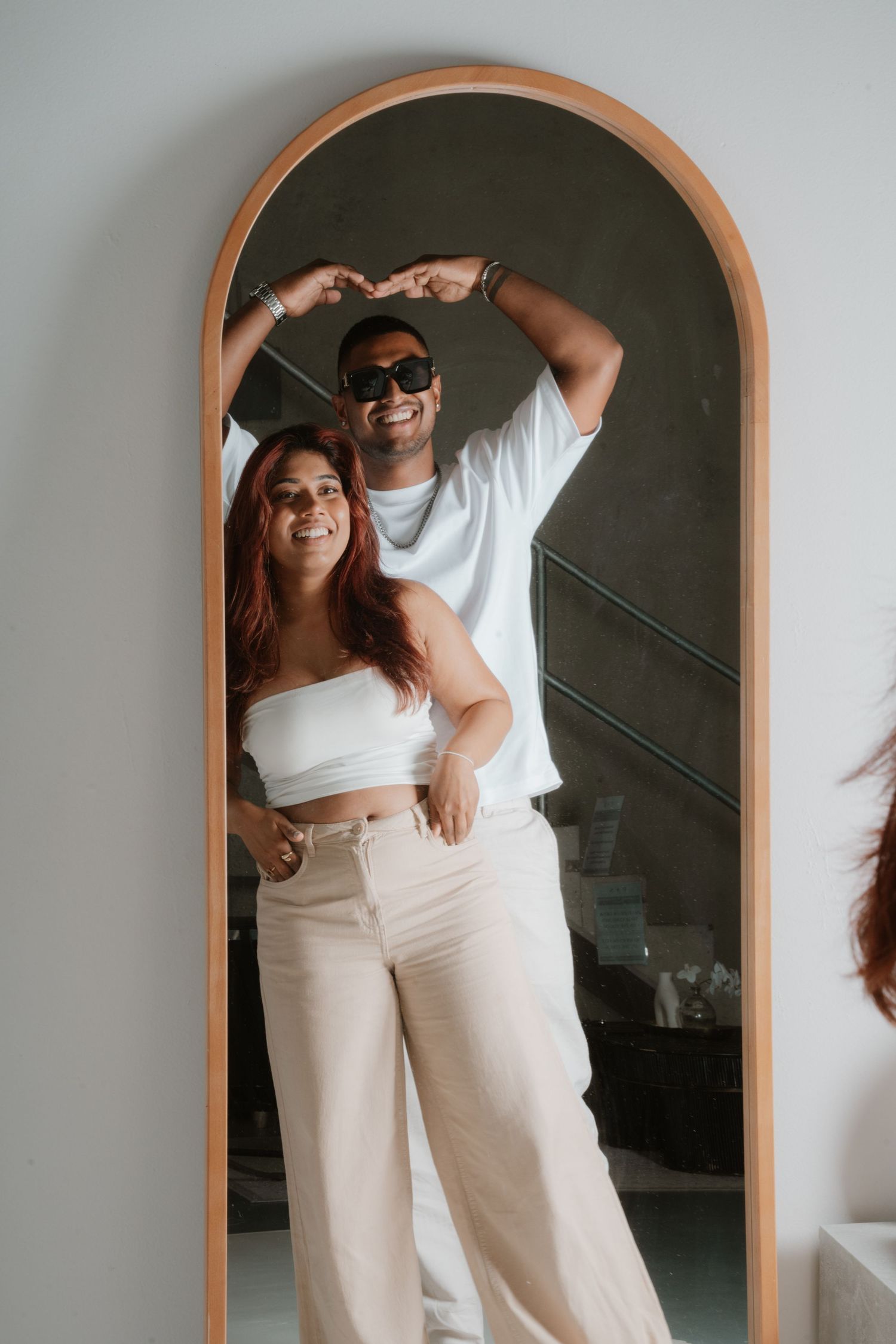 Smiling couple posing playfully in reflection of an arched floor mirror.