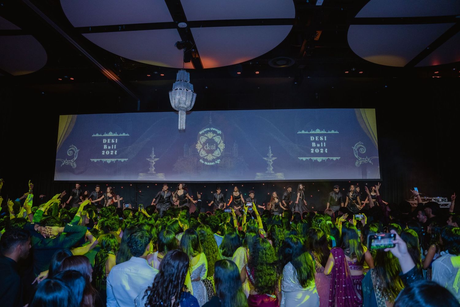Vibrant cultural celebration event with crowd dancing before a large illuminated stage backdrop.