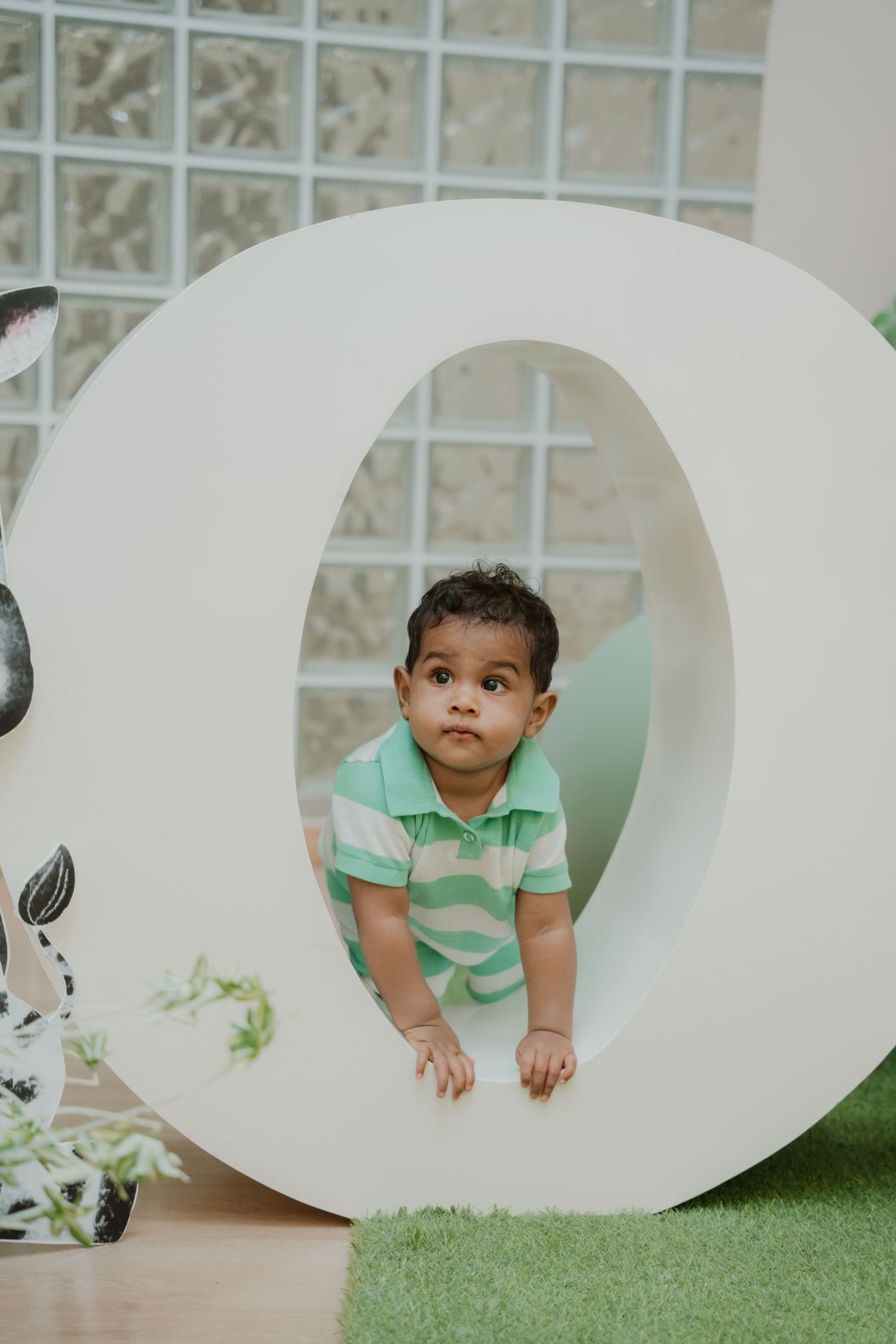 A curious baby peeks through a large white letter O at a safari-themed first birthday party celebration.