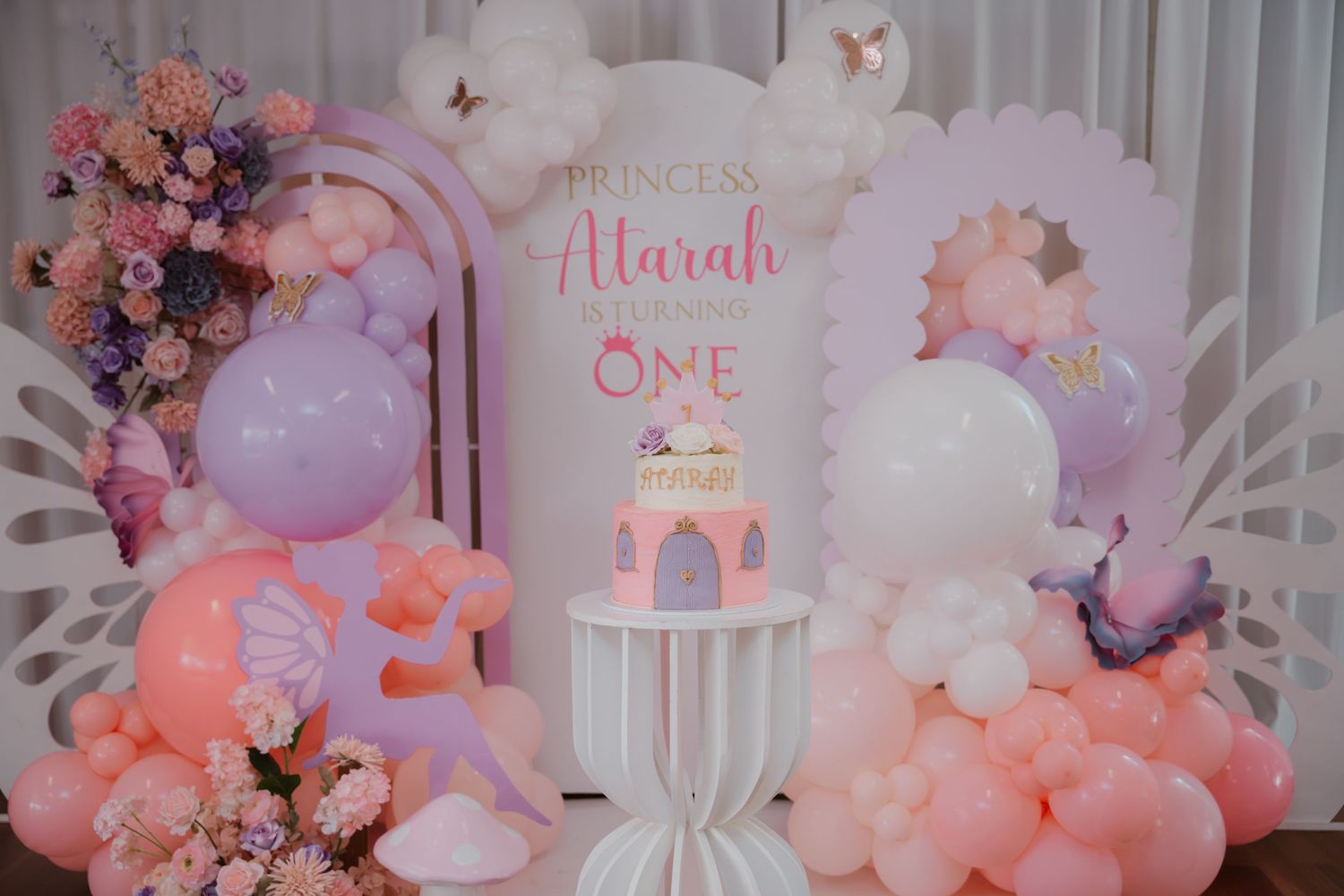 Pink and white princess birthday party backdrop with balloon arch and castle cake display.