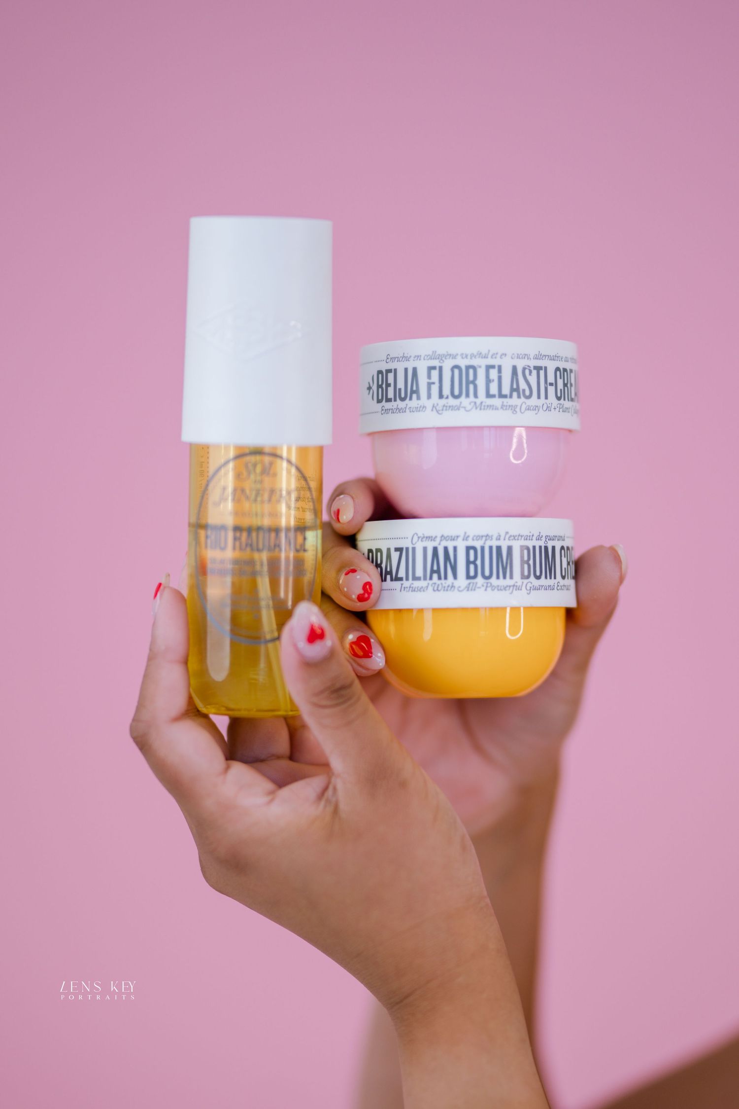 Hands holding Sol de Janeiro Brazilian Bum Bum Cream and body oil against a pink background.