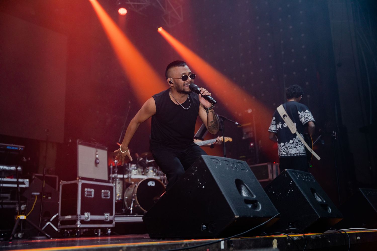 Male singer in black performs energetically on stage with red and orange stage lighting.