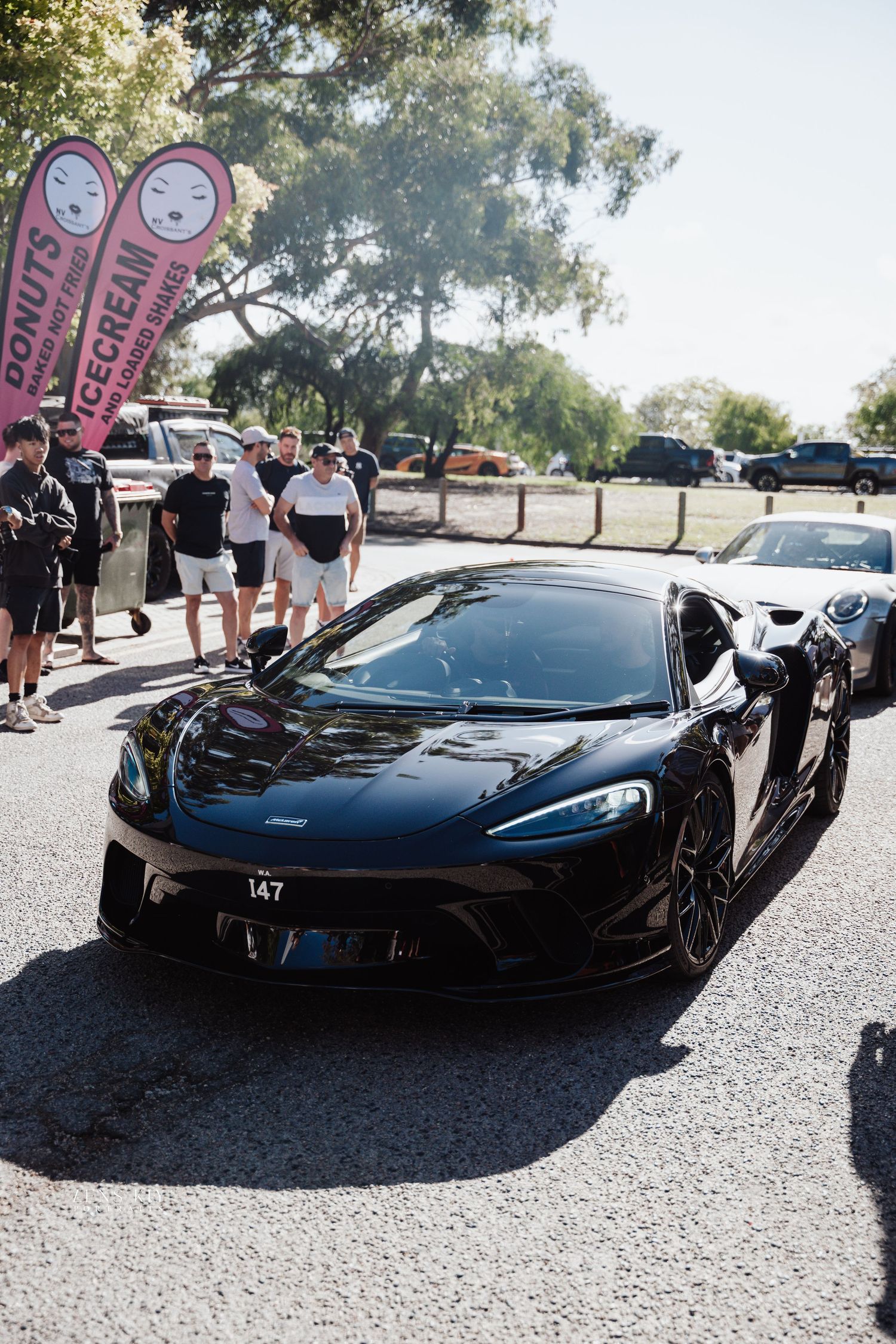 A black McLaren GT sports car on display at an outdoor car show with spectators nearby.