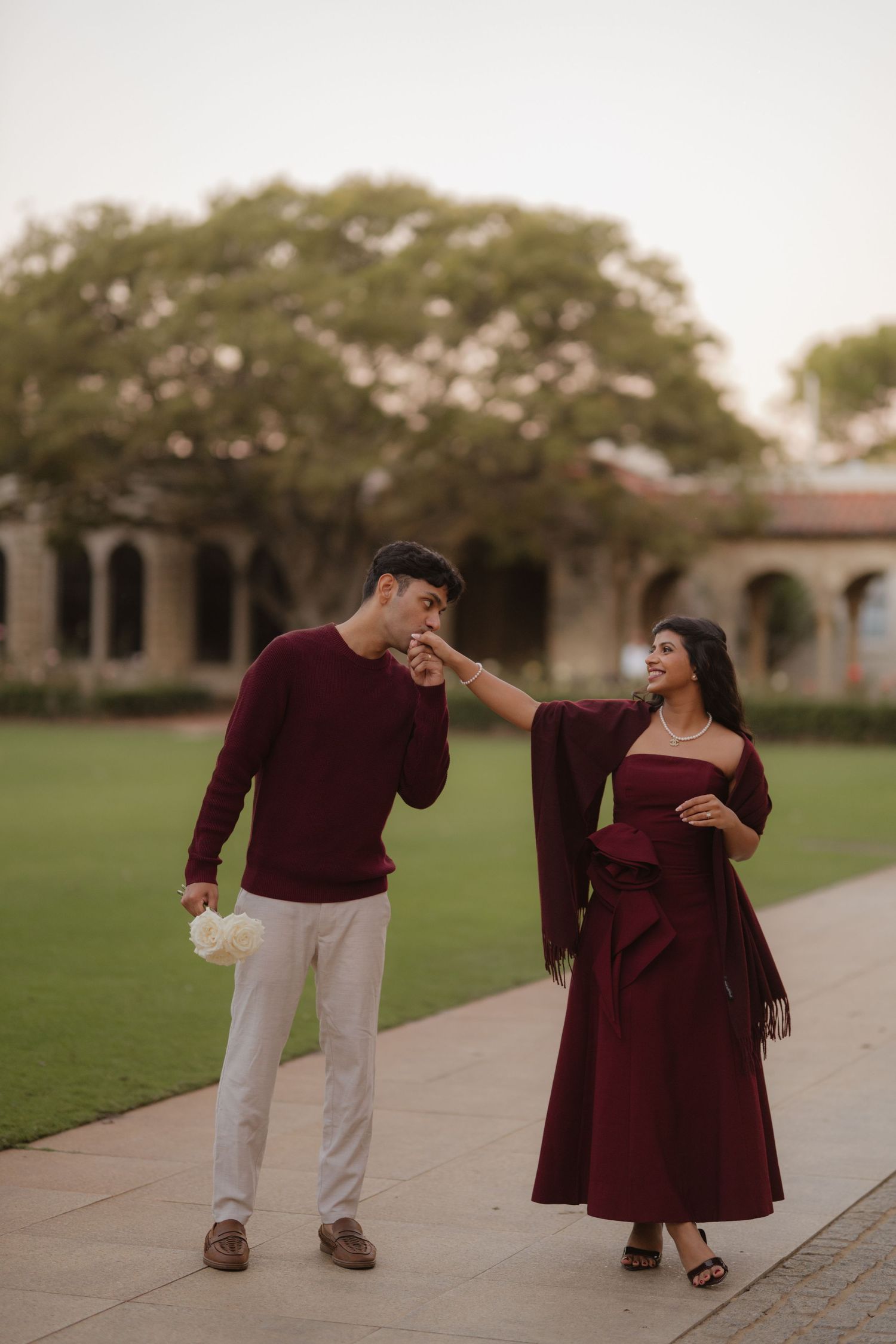 Couple in matching burgundy outfits share romantic moment as man kisses womans hand outdoors.