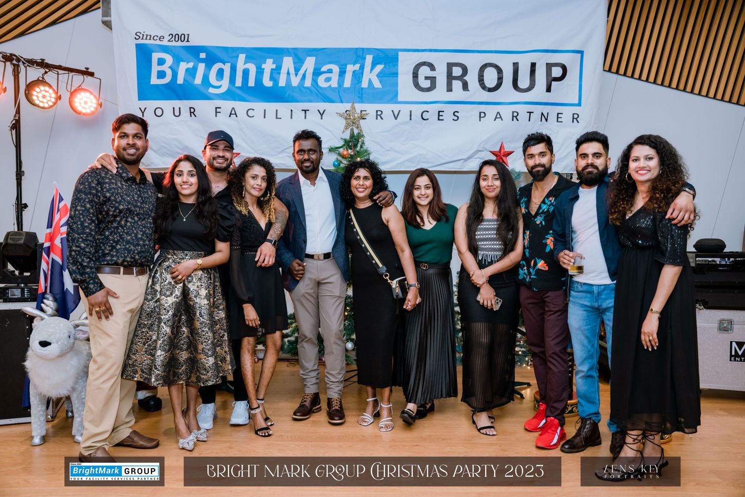 Group of ten colleagues posing at BrightMark Group Christmas Party 2023 with festive backdrop.