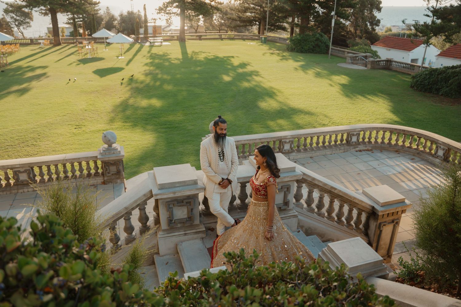 Aerial view of Indian wedding couple walking on stone terrace overlooking scenic green garden.