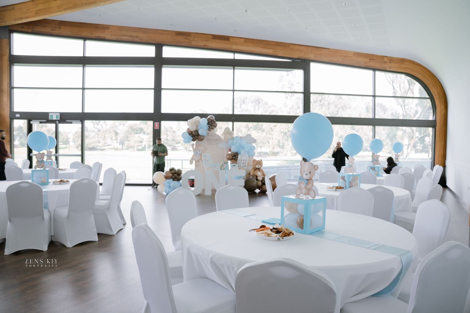 Elegant baby shower venue with white chairs, round tables, and blue balloon decorations.