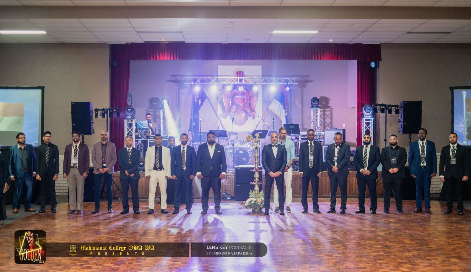 Group of formally dressed men standing on stage at a Sri Lankan college alumni event.