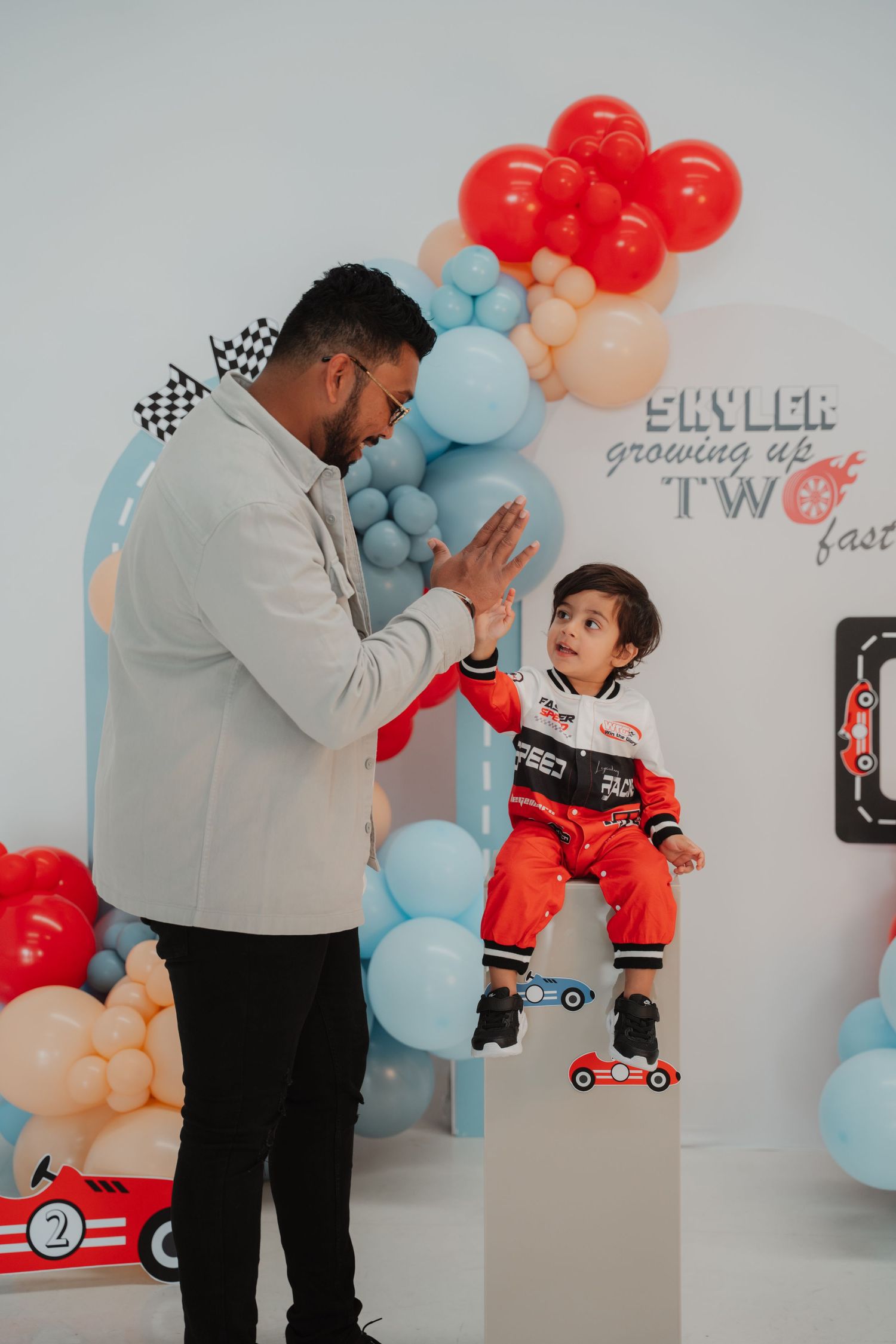 A father gives a high five to his toddler son at Skyler's race car themed second birthday celebration.