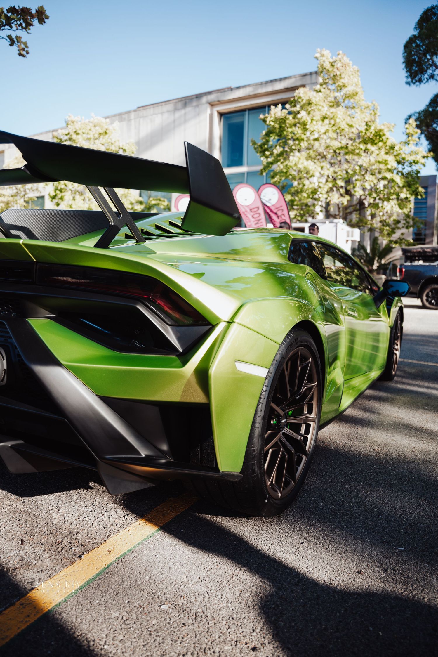 Vibrant green Lamborghini Huracan supercar with large rear wing parked on a sunny street.