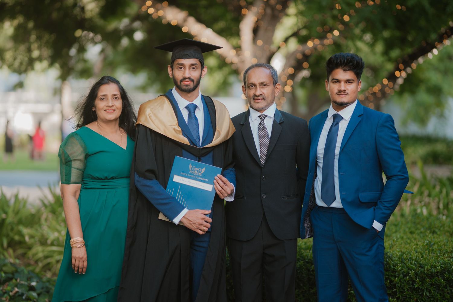 Graduate in black and gold academic gown with family of four posing outdoors at graduation.